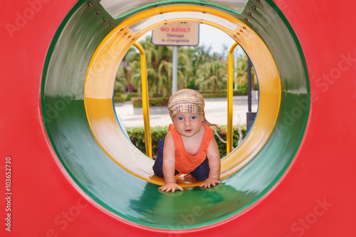 Smiling happy baby boy crawling with fun through colorful playground tube. Family lifestyles, outdoor recreational activity in parks on active summer holidays with child. © Tropical studio