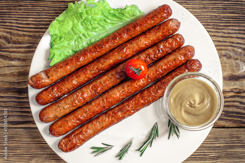 grilled sausages with tomato and rosmarine on plate at wooden photo