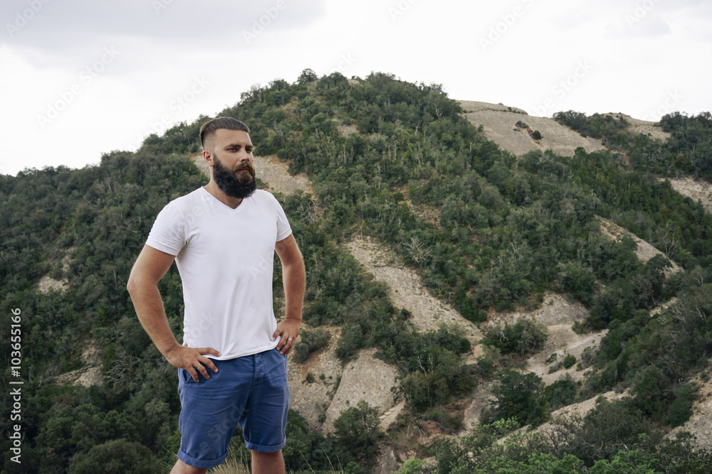 young man in a white t-shirt is enjoying a view of the top of the mountain