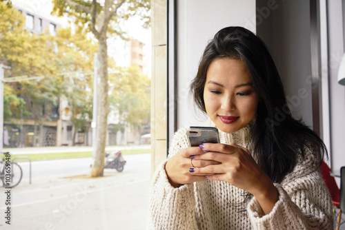 Young Asian Girl chatting via digital tablet device during breakfast in coffee shop.Portrait of a pretty Asian woman reading message on her cell telephone