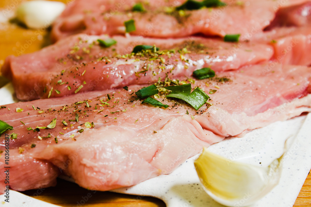 Sliced pork on a white board sprinkled with salt, Italian herbs and onion. Raw pork prepared to cook. Sliced pork on a white board sprinkled with salt, Italian herbs and onion. Raw pork prepared to cook.
