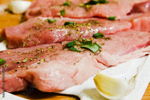 Sliced pork on a white board sprinkled with salt, Italian herbs and onion. Raw pork prepared to cook.