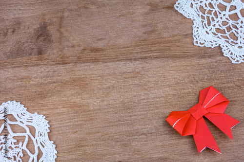 Origami red bow on a wooden background with lace.