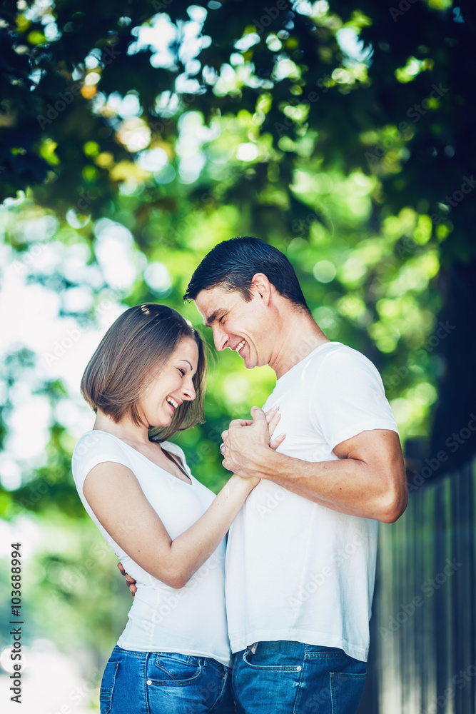 Portrait of beautiful couple man woman in love wearing white tshirt and jeans outside holding hands, hugging, smiling laughing looking away from camera, toned with Instagram filters, film movie effect