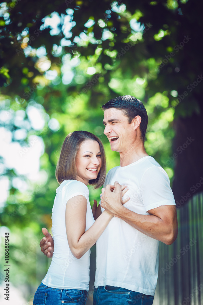 Portrait of beautiful couple man woman in love wearing white tshirt and jeans outside holding hands, hugging, smiling laughing looking away from camera, toned with Instagram filters, film movie effect Portrait of beautiful couple man woman in love wearing white tshirt and jeans outside holding hands, hugging, smiling laughing looking away from camera, toned with Instagram filters, film movie effect