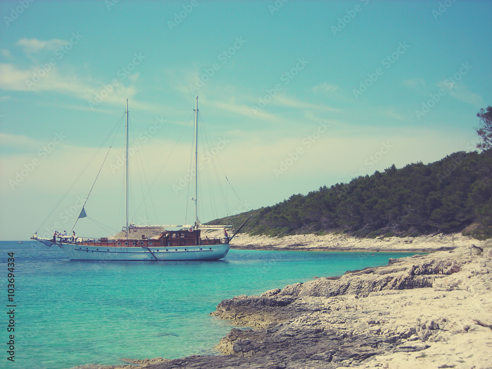 White rocky beach, clear blue sea and a moored boat, on a sunny day. Image filtered in faded, retro, Instagram style with extremely soft focus; nostalgic, vintage concept of summer holidays.