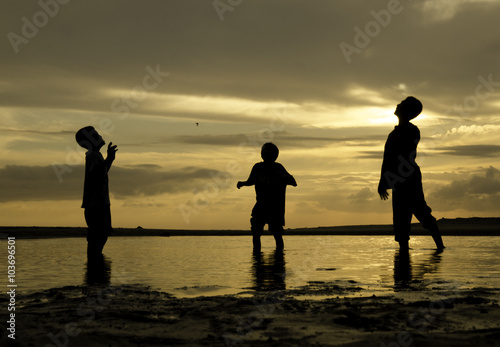 silhouette image of three boys playing at the beach with beautiful sunrise background.