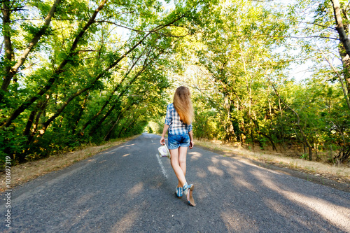 beautiful girl walking on an empty road between green trees