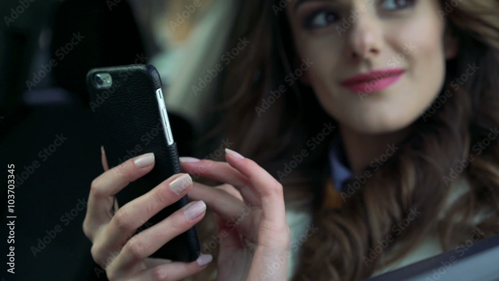 Girl sitting in the car using phone, smiling and looking through the window Girl sitting in the car using phone, smiling and looking through the window
