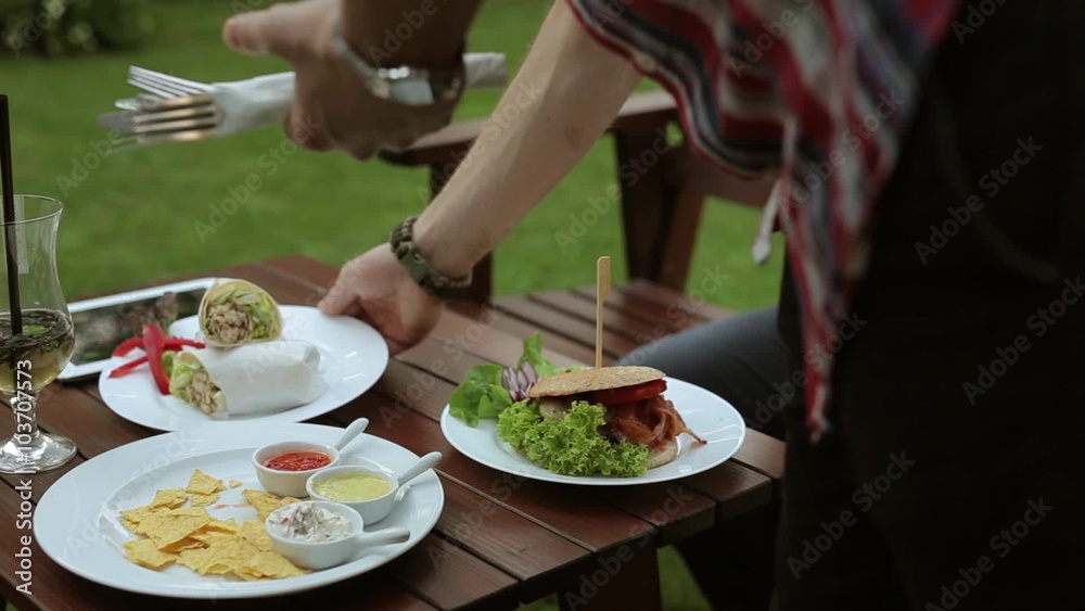 Man sitting behind the table and texting messages on his phone. During this time waitress brings him hamburger Man sitting behind the table and texting messages on his phone. During this time waitress brings him hamburger