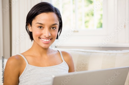 Smiling brunette using laptop on the sofa