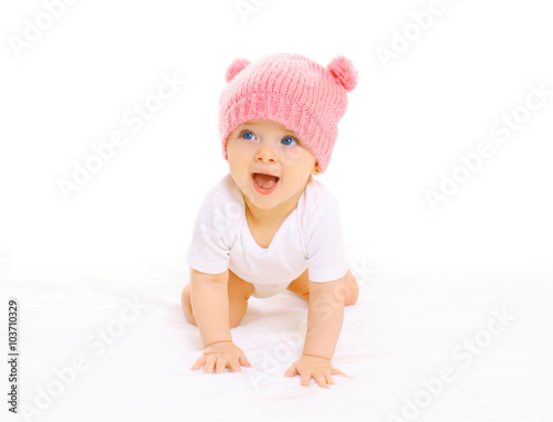 Happy cute smiling baby in knitted pink hat crawls on a white ba