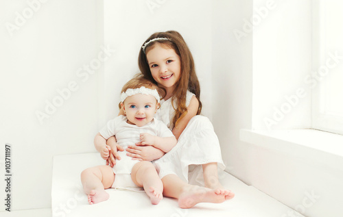 Two sisters children playing together at home in white room