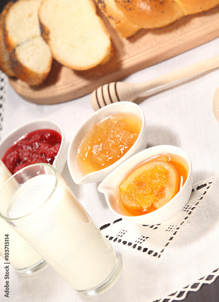White bowls with homemade jams next to a glass of milk and sweet baked bun are on linen tablecloth on a rustic table White bowls with homemade jams next to a glass of milk and sweet baked bun are on linen tablecloth on a rustic table