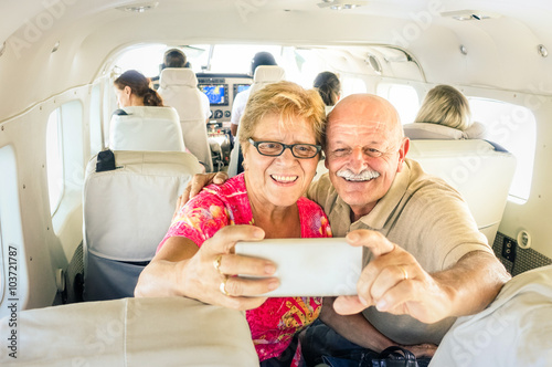 Senior happy couple taking selfie with mobile phone on board of plane  -  Smiling retired people having fun flying from Coron to Borakay  - Concept of elderly happiness on world wide travel 