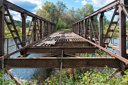 Disturbed rusty steel bridge above river in diminishing perspective. Nikolo-Uryupino village, Moscow regon, Russia.
 photo