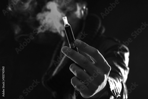 Hand holding an electronic cigarette over a dark background black and white