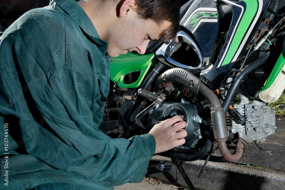 Teenage mechanic working on a motorbike - obrazy, fototapety, plakaty 