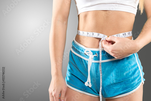 sport, fitness and diet concept - close up of trained belly with measuring tape