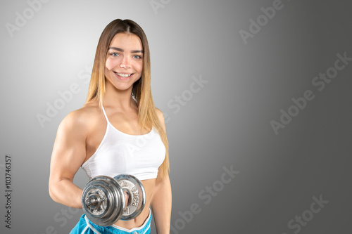 muscular female wearing sports clothes working out with dumbbell