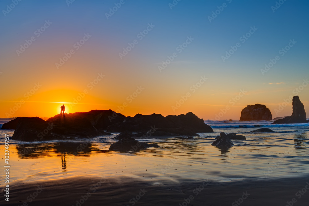Photograper shooting sunset at Bandon Beach over the Pacific ocean with reflections on wet sand, Bandon, Oregon