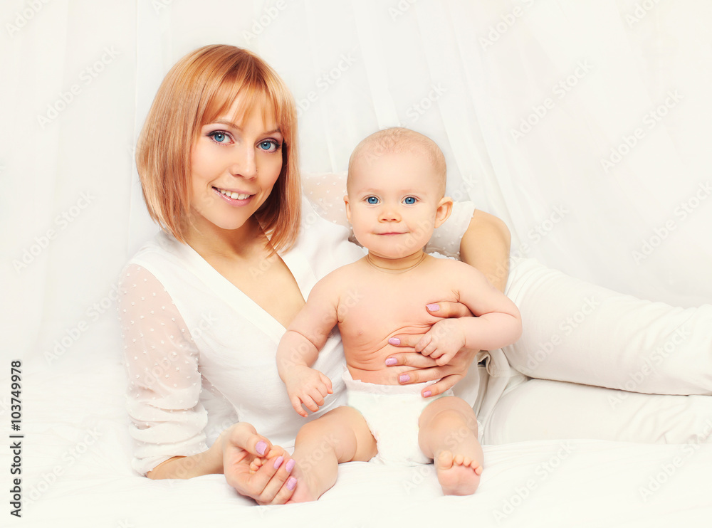 Happy smiling mother with baby lying together on bed at home Happy smiling mother with baby lying together on bed at home