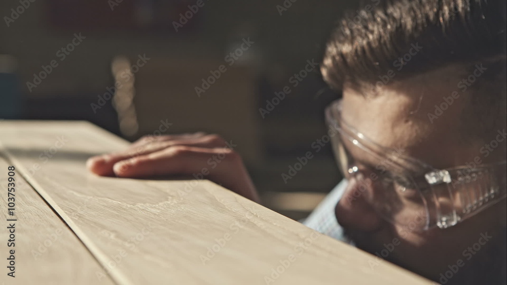 A young bearded carpenter checks the quality of the boards in the sun. RAW video record.