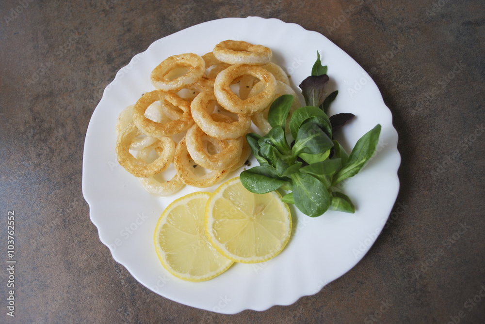 Cooked squid rings with green salad and lemon on white dish. Cooked squid rings with green salad and lemon on white dish.