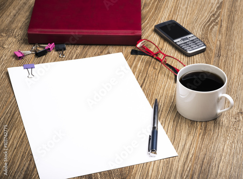 View Of An Office Desk With Calendar, Cell Phone, Coffee Cup, Sheet Of Paper For Notice, Glasses And Pen.