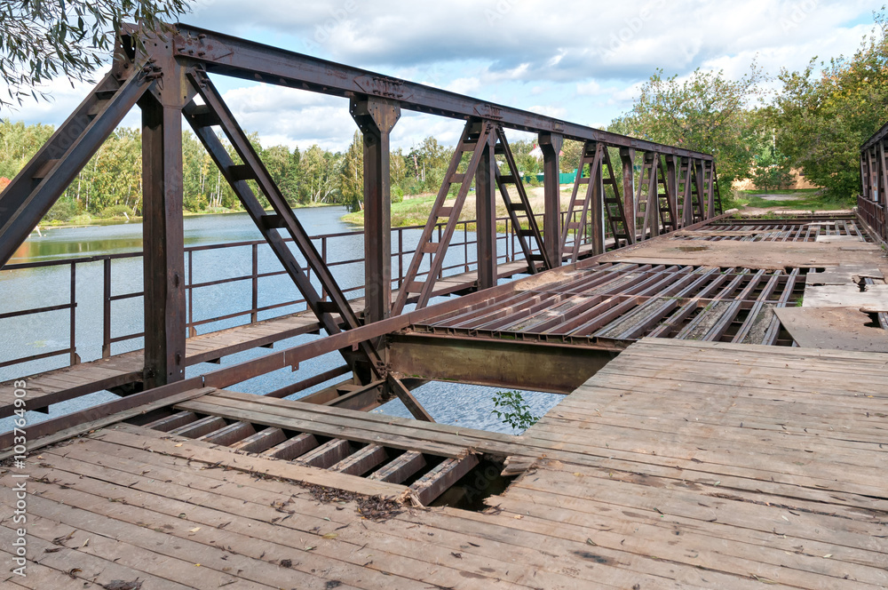 Disturbed rusty steel bridge above river in diminishing perspective. Nikolo-Uryupino village, Moscow region, Russia.
