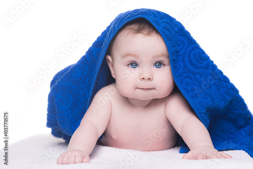 baby with big blue eyes looking at camera under blue towel/blank