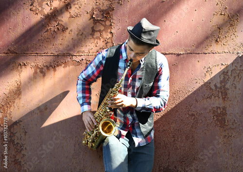 Young man playing on saxophone outside near the old wall