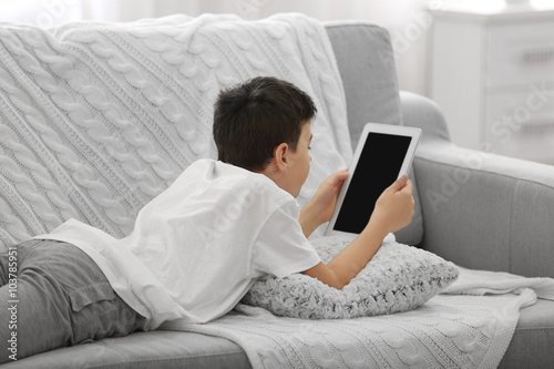 Boy using tablet on a sofa ...