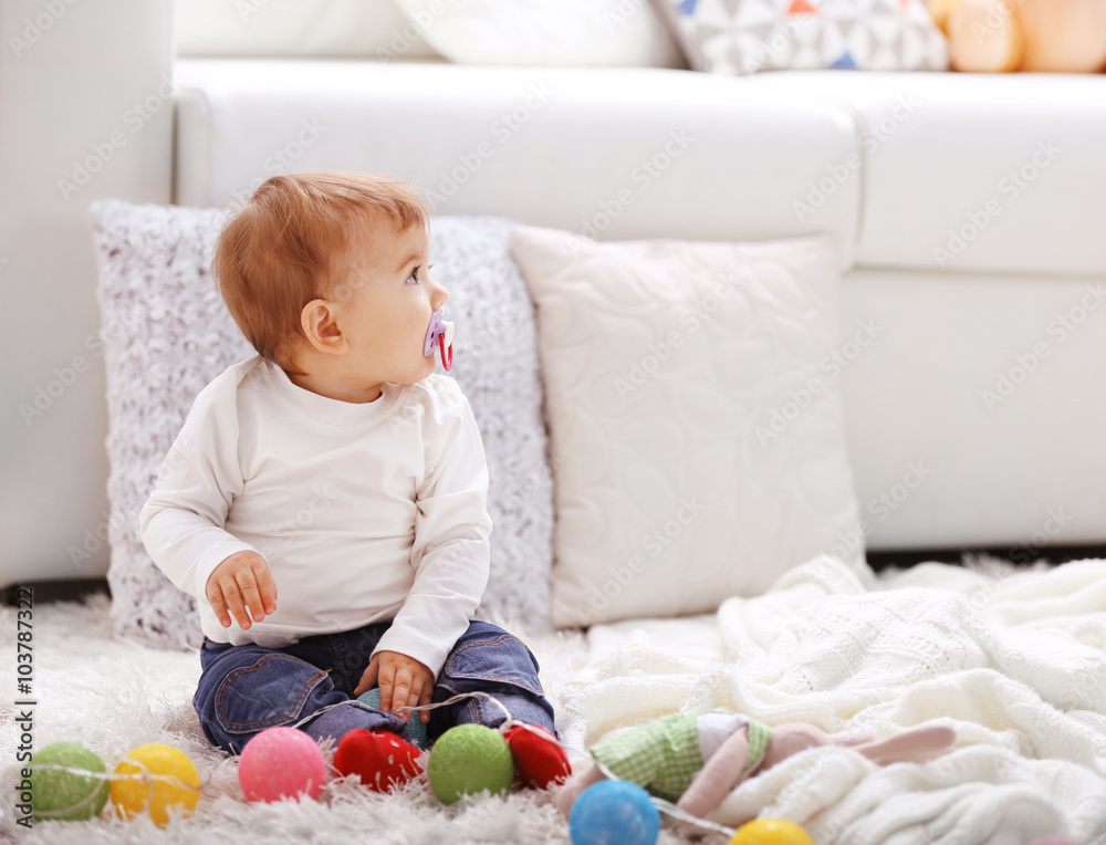 Naklejka premium Sweet baby girl with a soother playing on a floor
