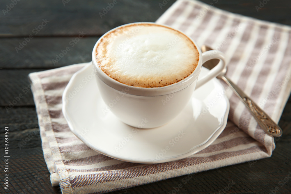 Cup of hot cappuccino with froth and spoon on a black wooden table Cup of hot cappuccino with froth and spoon on a black wooden table