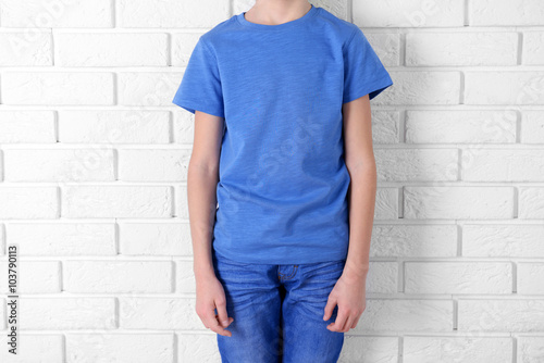 Clothes advertising. Boy in blue T-shirt and jeans on white brick wall background, close up