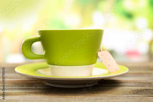 Green cup with tea bag on wooden table, close up