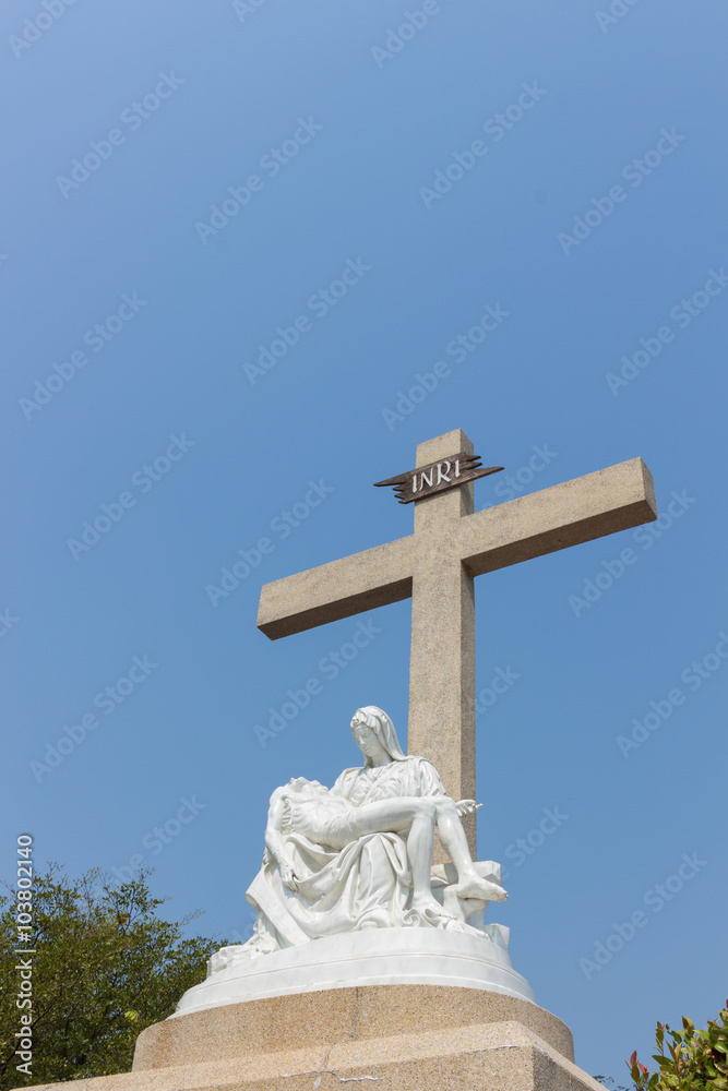 Pieta statue with cross and sky background