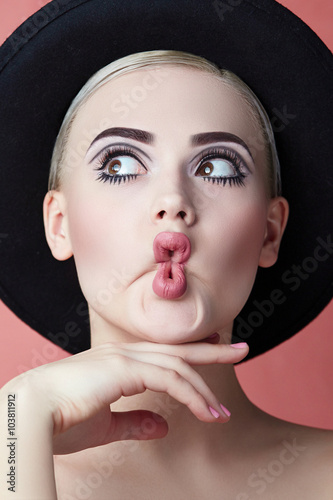 Portrait of a girl in a black hat on a pink background with a graphic quality makeup and hair combed. photo