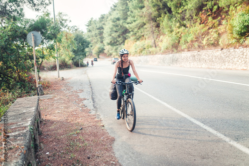 Young pretty woman with backpack and helmet travels with bicycle outdoors on the asphalt road © EdNurg