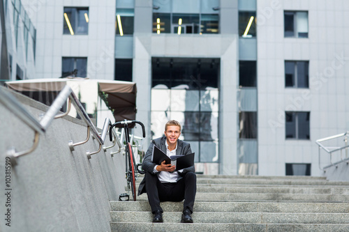 a young businessman standing on the steps of an office building, with a folder of papers and bike