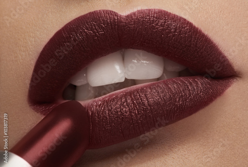 Fotografie Applying red lipstick on lips in close up photo