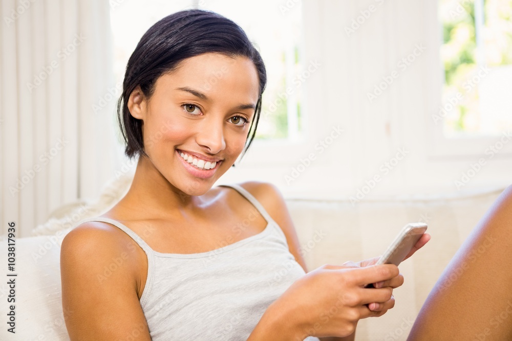 Smiling brunette using smartphone on the sofa Smiling brunette using smartphone on the sofa