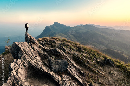 businessman hike on the peak of rocks mountain at sunset, succes photo
