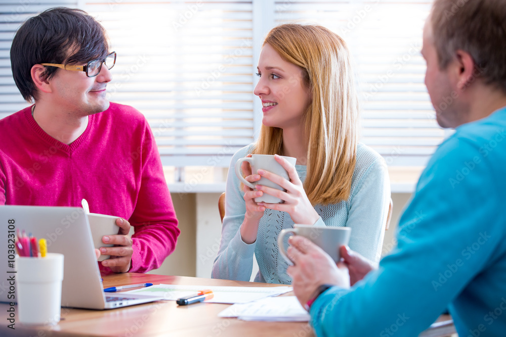 Young people discussing projects and ideas sitting around table with laptop. Group of young colleagues having a meeting at office. Coffee break Young people discussing projects and ideas sitting around table with laptop. Group of young colleagues having a meeting at office. Coffee break