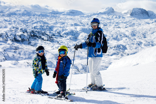 Father and two boys, skiing on a sunny day on a mountain summit
