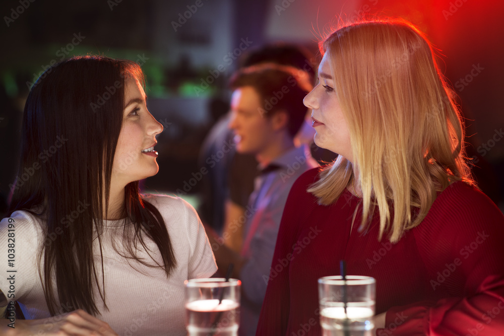 Two attractive girls having a intensive conversation at the bar with a drink in their hands Two attractive girls having a intensive conversation at the bar with a drink in their hands