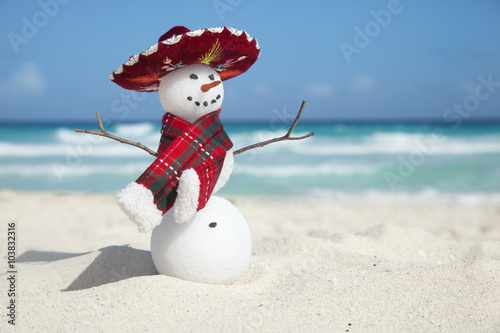 Miniature snowman wearing Mexican sombrero and scarf on the beac