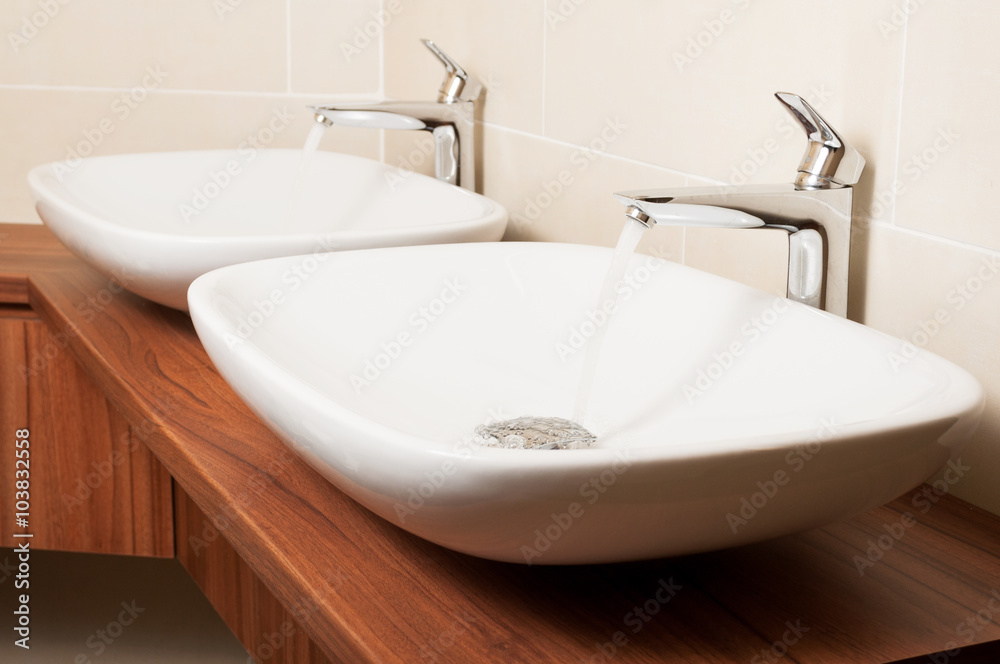 Close-up of shiny taps with flowing water and ceramic sinks Close-up of shiny taps with flowing water and ceramic sinks
