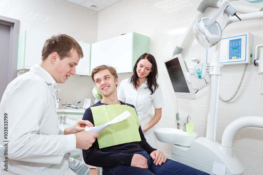 Obraz premium Male dentist and taking notes, with happy patient, at the dental office.
